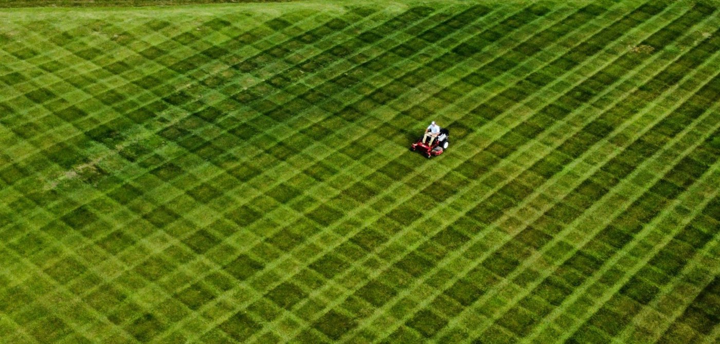 Aerial view of a riding mower cutting a large field in a crosshatch pattern